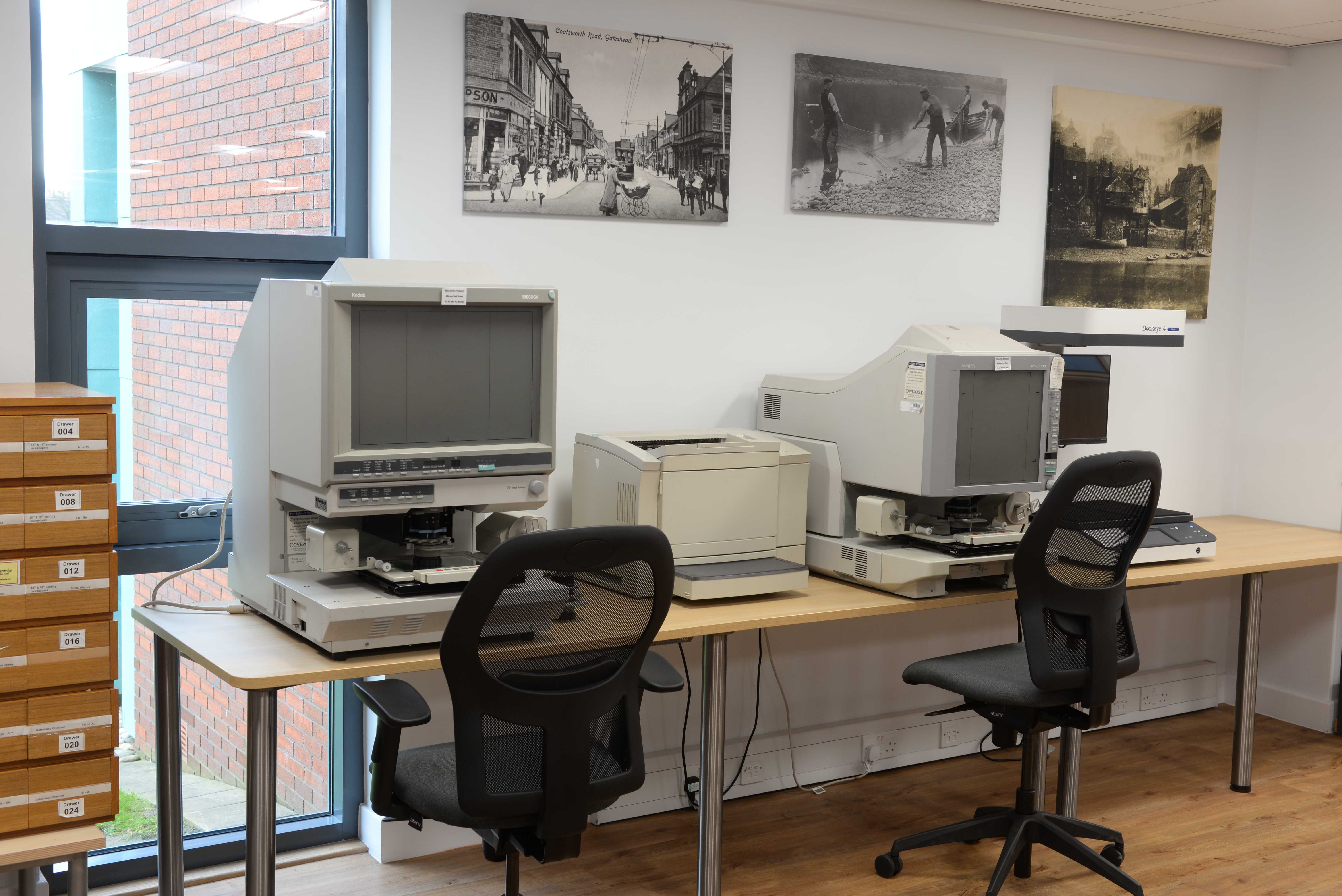 Canvas prints of early photographs decorate walls above microfilm readers